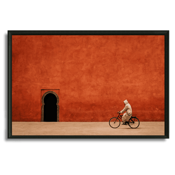Tableau marocain cycliste en djellaba devant mur rouge et arche traditionnelle